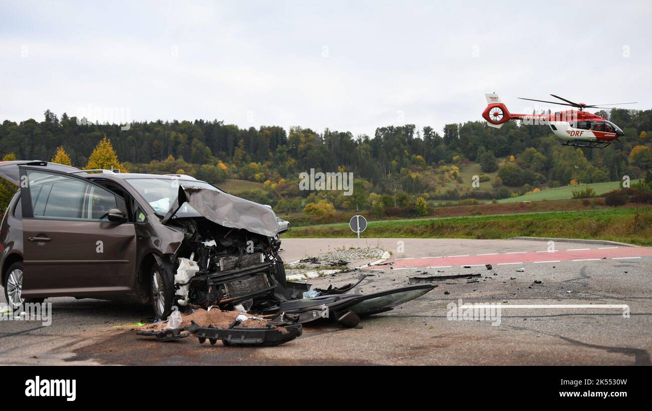 Fichtenberg, Germany. 06th Oct, 2022. A badly damaged car stands on a road; a rescue helicopter can be seen in the background in the air. Seven schoolchildren were slightly injured in an accident between a minibus and a car. The minibus was thrown about 20 meters and came to rest on its side. The driver of the car was seriously injured. (To 'Seven children slightly injured in bus accident') Credit: Jason Tschepljakow/onw-images/dpa/Alamy Live News Stock Photo