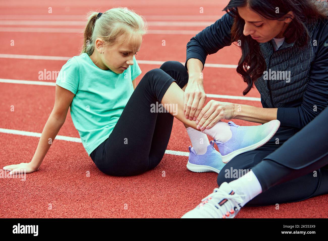 First aid for a young athlete at stadium. Sport teen girl suffering