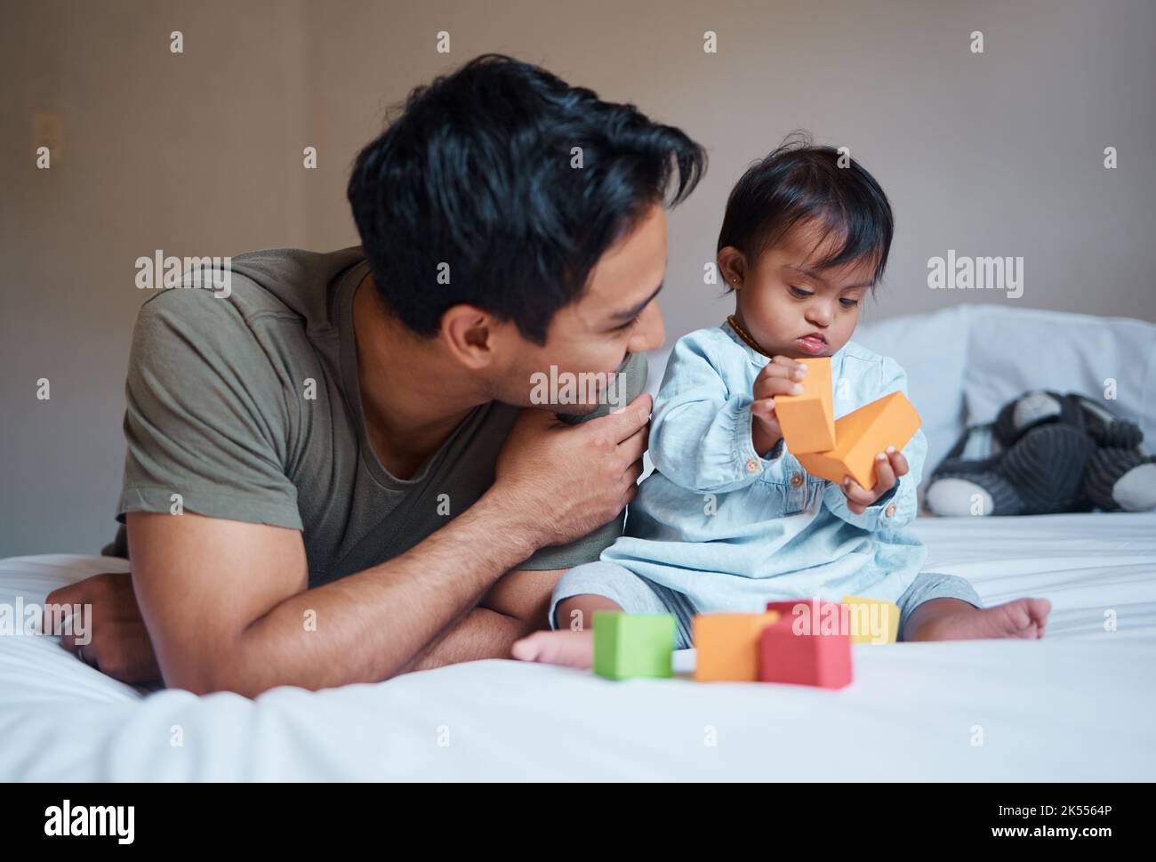 Father and down syndrome baby play education game with toys on bed for