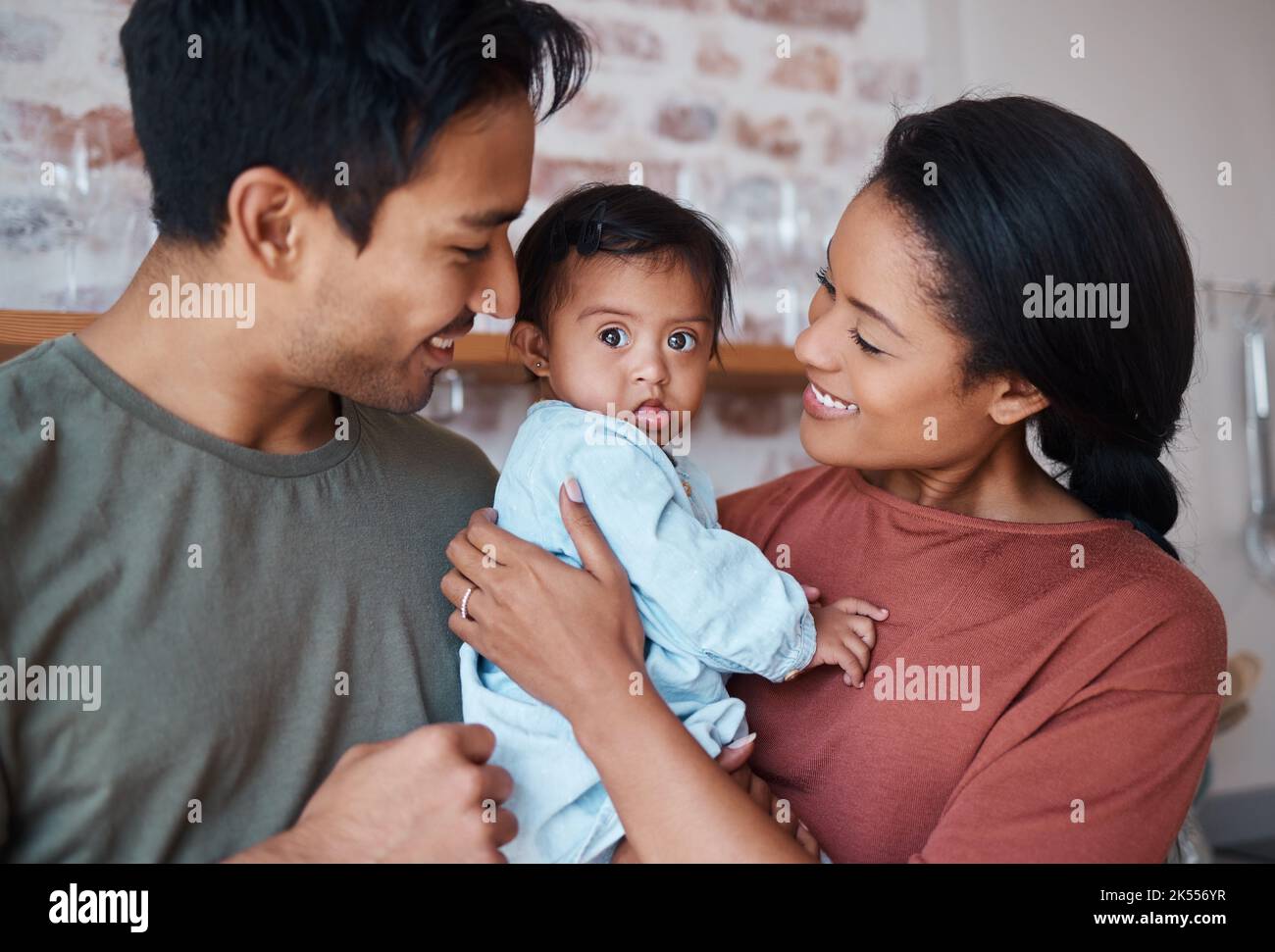 Love, happy parents and baby with down syndrome in the kitchen embracing and bonding in their home. Happiness, smile and family care with special Stock Photo