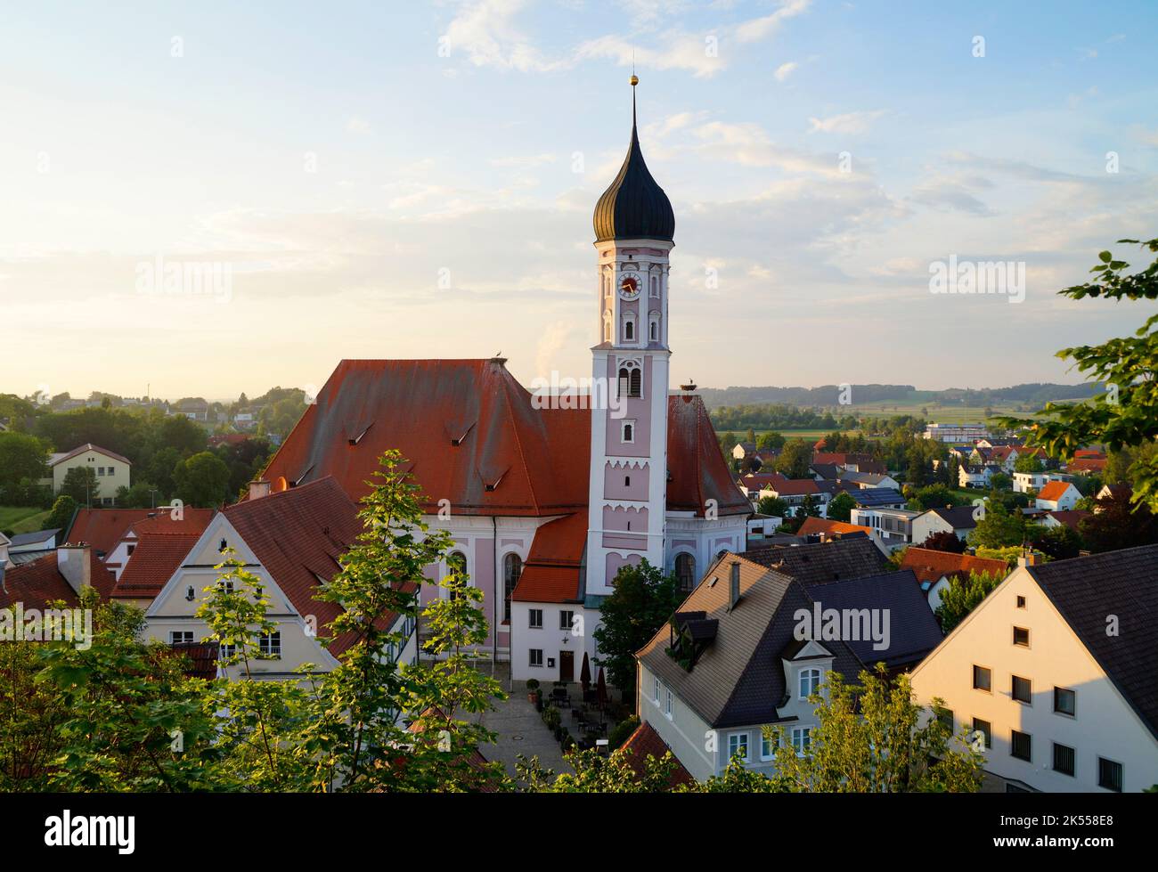 a beautiful old church in Burgau with an askew tower surrounded by the old quaint houses und lush green trees on a sunny summer day, Bavaria Stock Photo