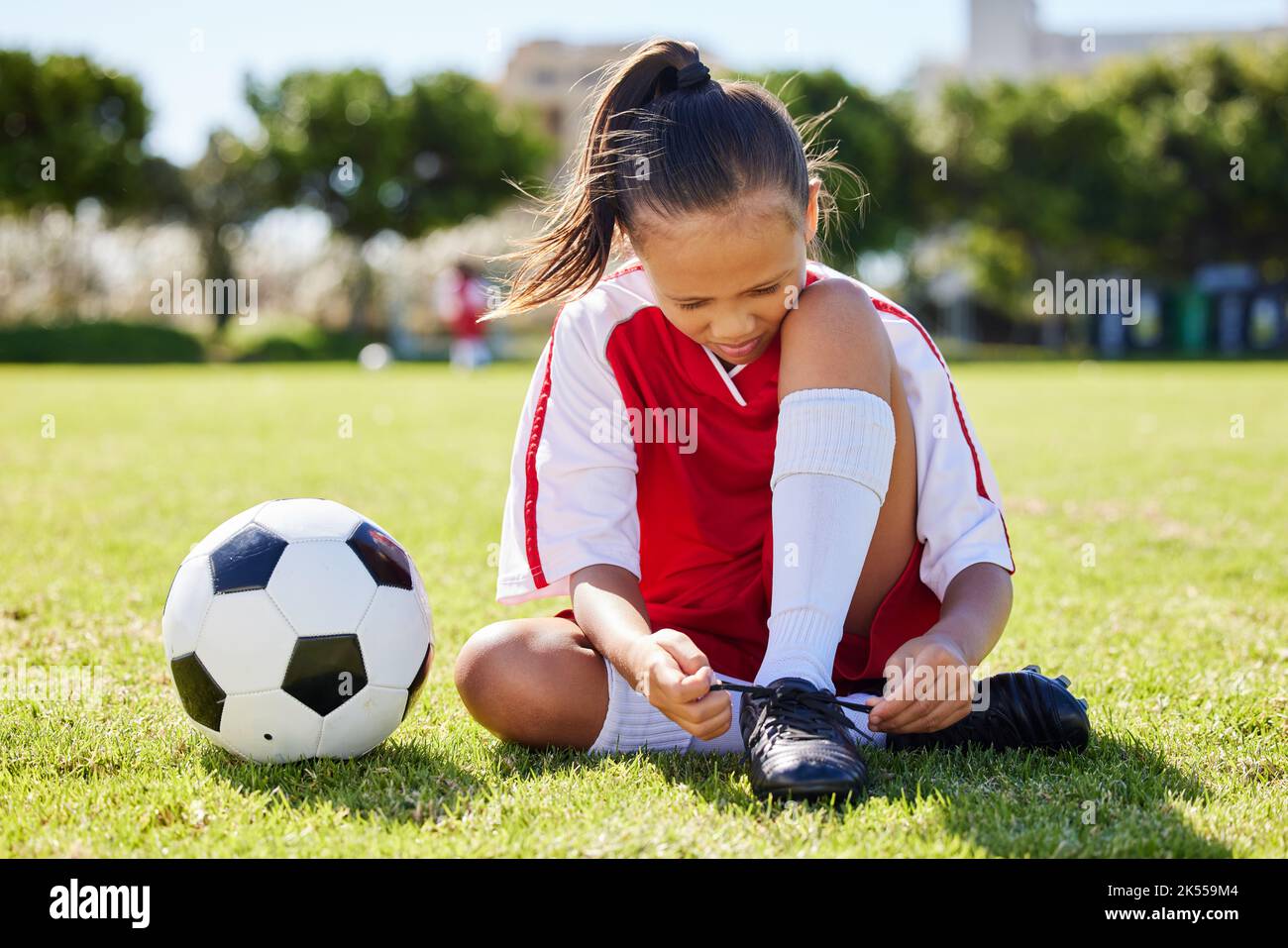 Sports, soccer and tie shoes with girl on grass for fitness, games and training in brazil event. Motivation, workout and exercise with young child on Stock Photo