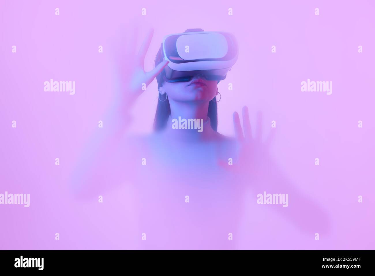 Virtual reality. Young girl in VR eyewear, immersed in clouds of smoke, fog on a pink neon background with a backlight diffuser. Stock Photo