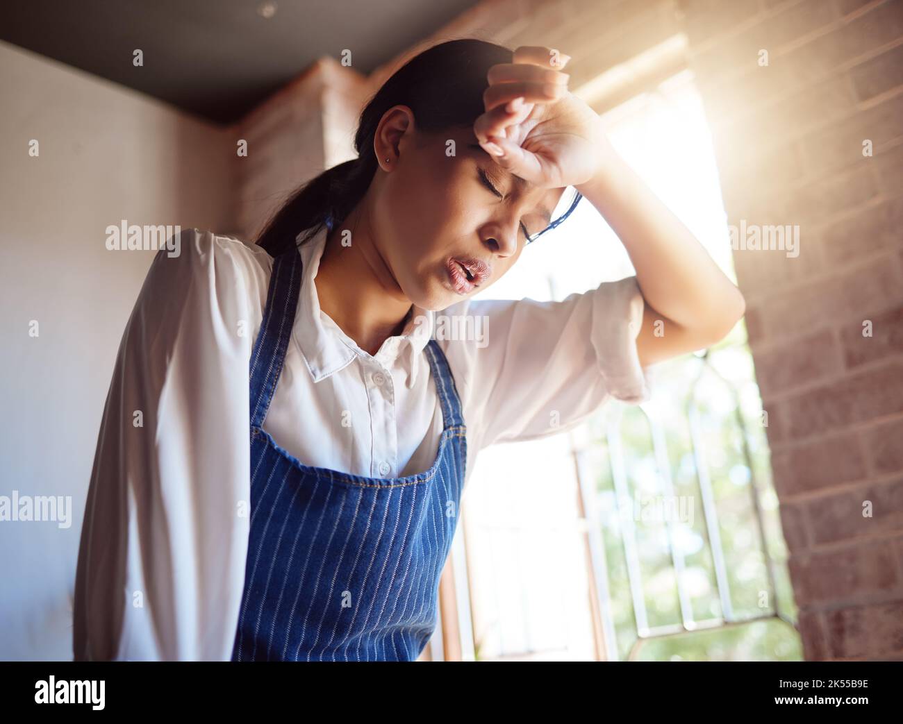 Woman, tired and apron tired from working in cafe, home or cooking job. Girl, chef and cook with headache from cooking burnout or work for service in Stock Photo