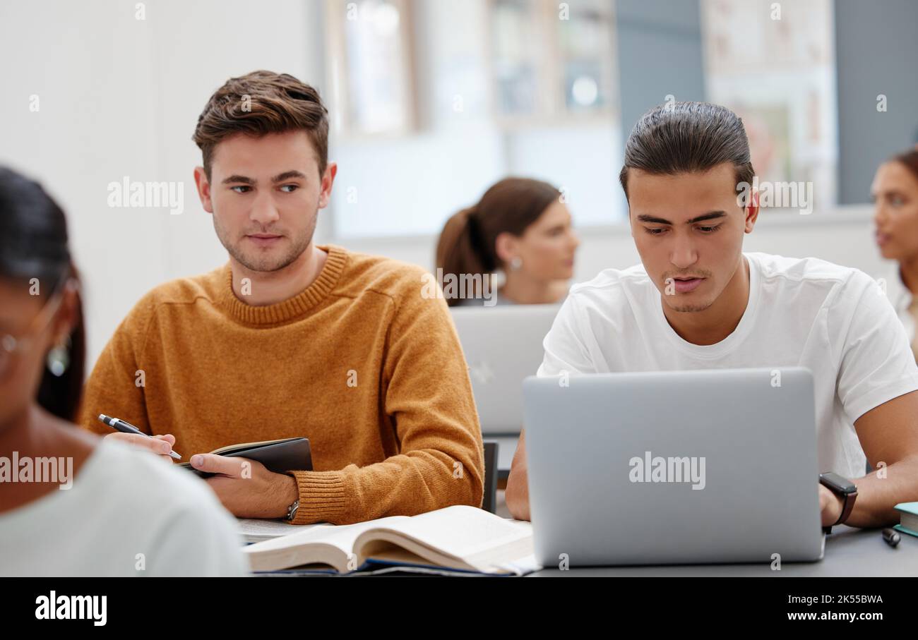 Education, laptop and student cheating in classroom working on test, exam or research. University, learning and college man writing notes, assignment Stock Photo