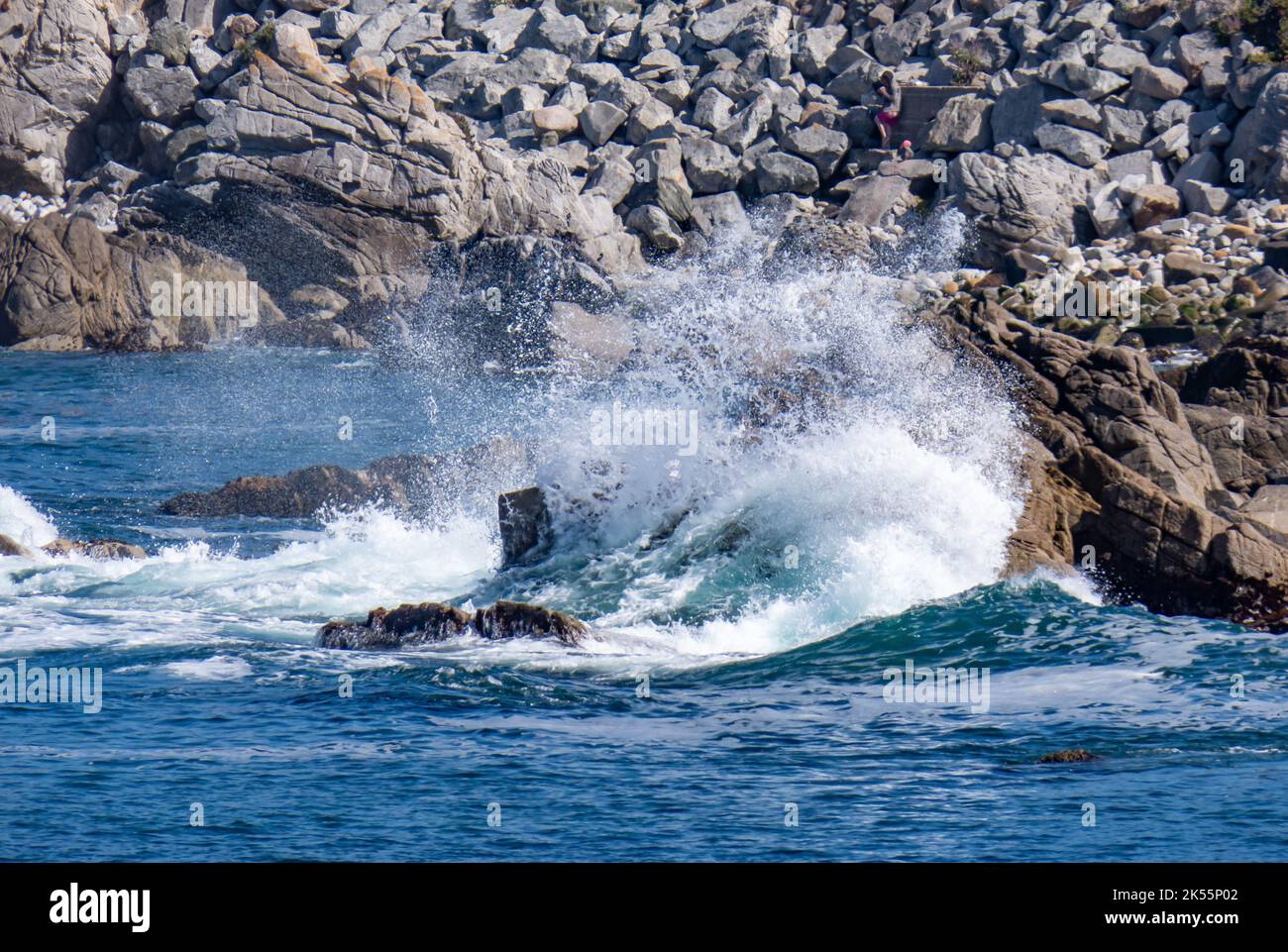 An Ocean wave crashing against rocks on a bright sunny day Stock Photo ...