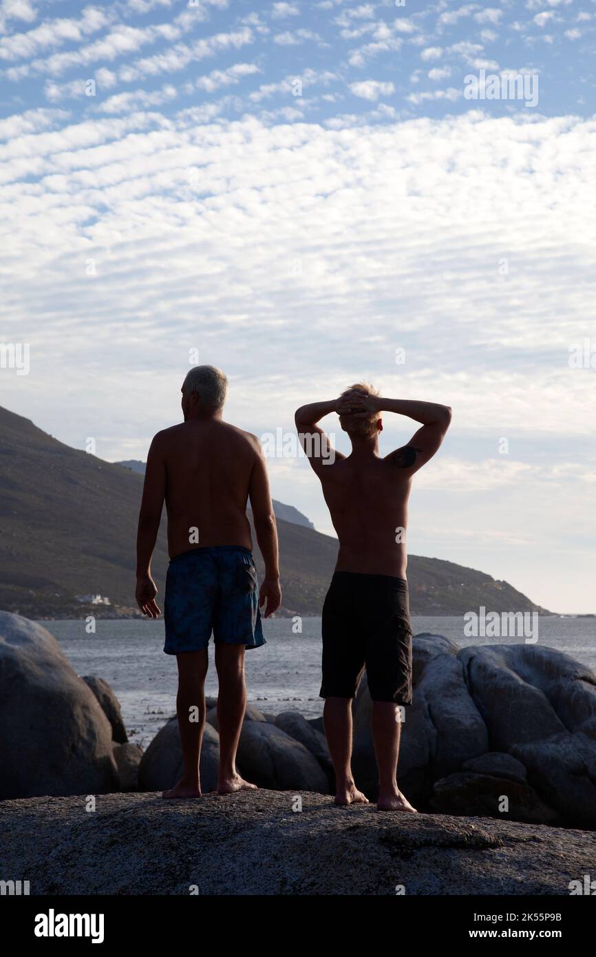 Two men on Rocks at Bakoven Beach at Sundow in Cape Town, South Africa Stock Photo