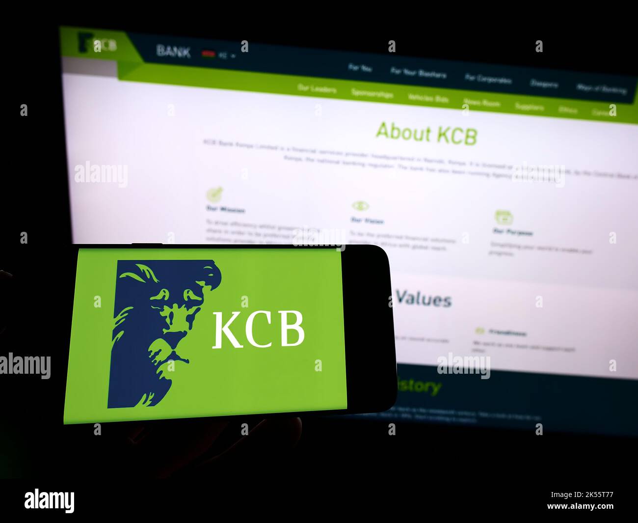 Person holding cellphone with logo of Kenyan financial company KCB Group Limited on screen in front of business webpage. Focus on phone display. Stock Photo