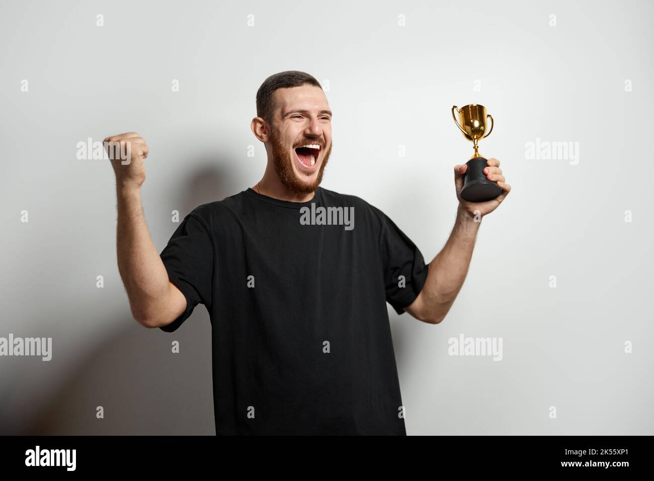 Happy young male or businessman holding his gold trophy and celebrating victory. Studio shot of man with cup as winner. Concept of win, success, human Stock Photo