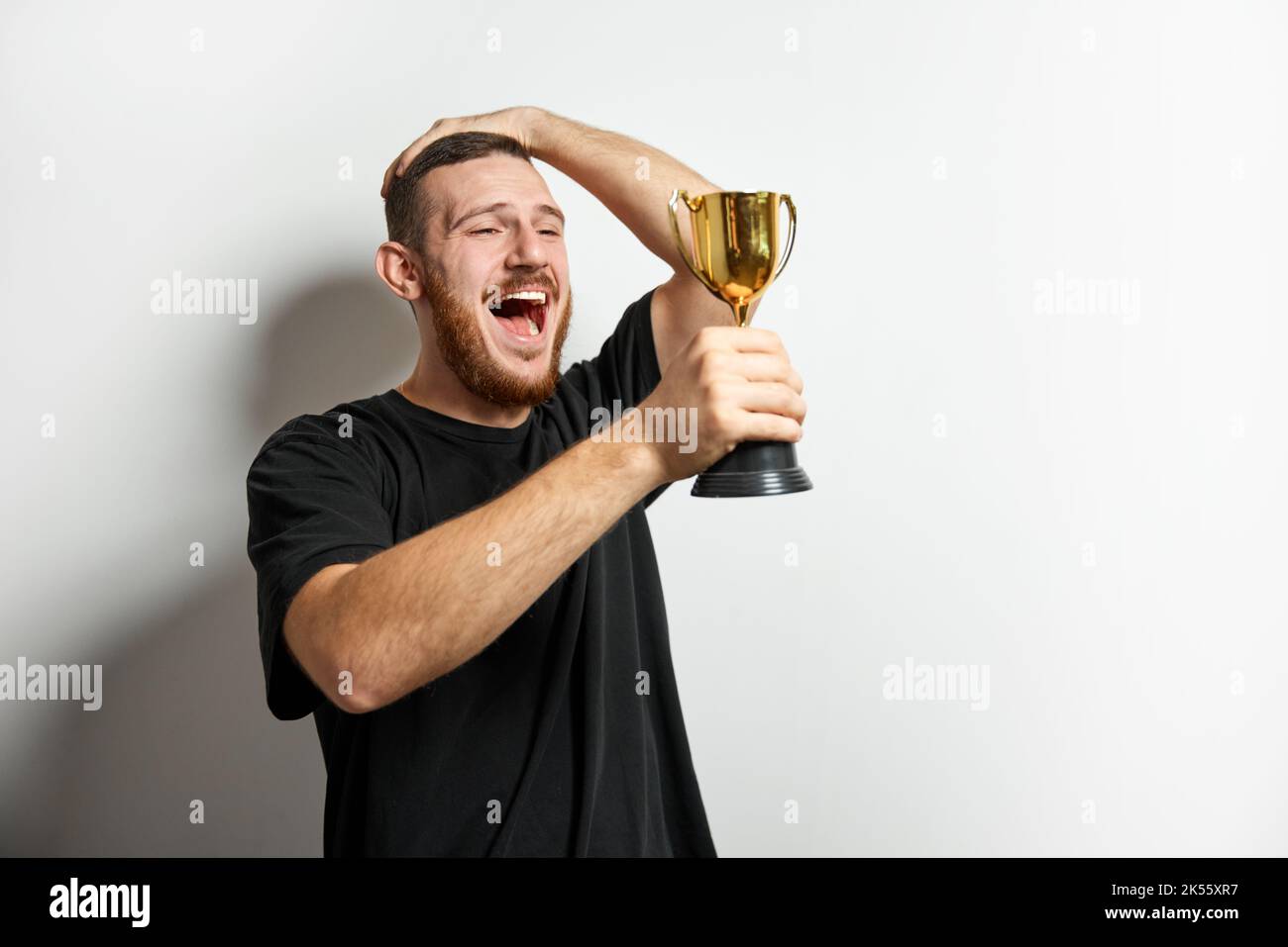Happy young male or businessman holding his gold trophy and celebrating victory. Studio shot of man with cup as winner. Concept of win, success, human Stock Photo
