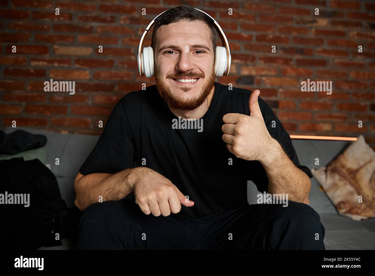 Handsome bearded man in headphones listening to music at home. Music. Half-length portrait of young guy in casual youth style clothes with sign ok Stock Photo