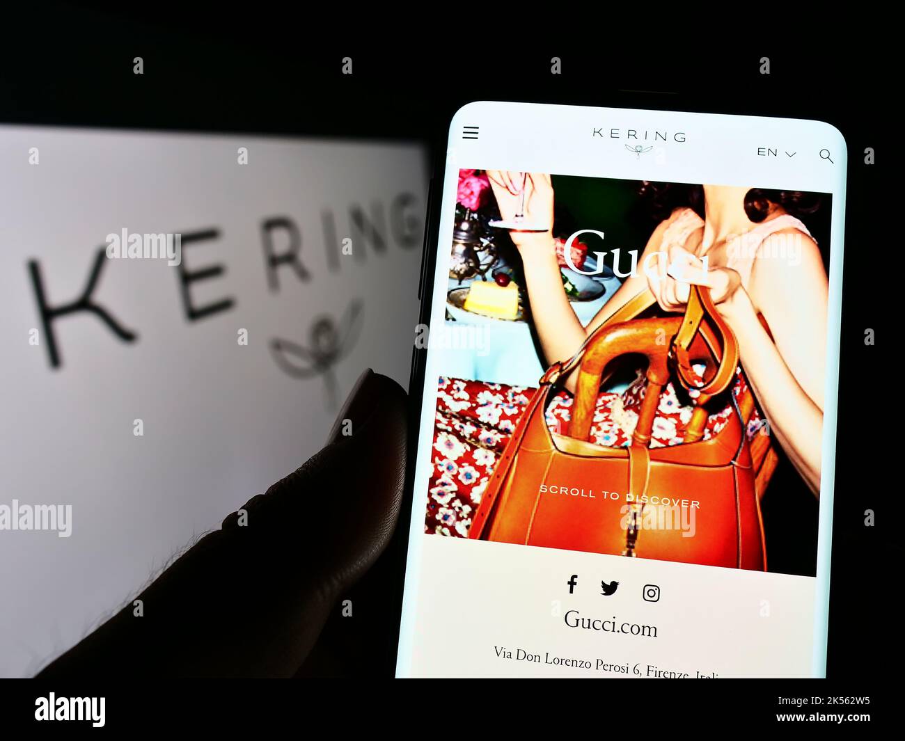 Person holding smartphone with webpage of French luxury goods company Kering S.A. on screen in front of logo. Focus on center of phone display. Stock Photo