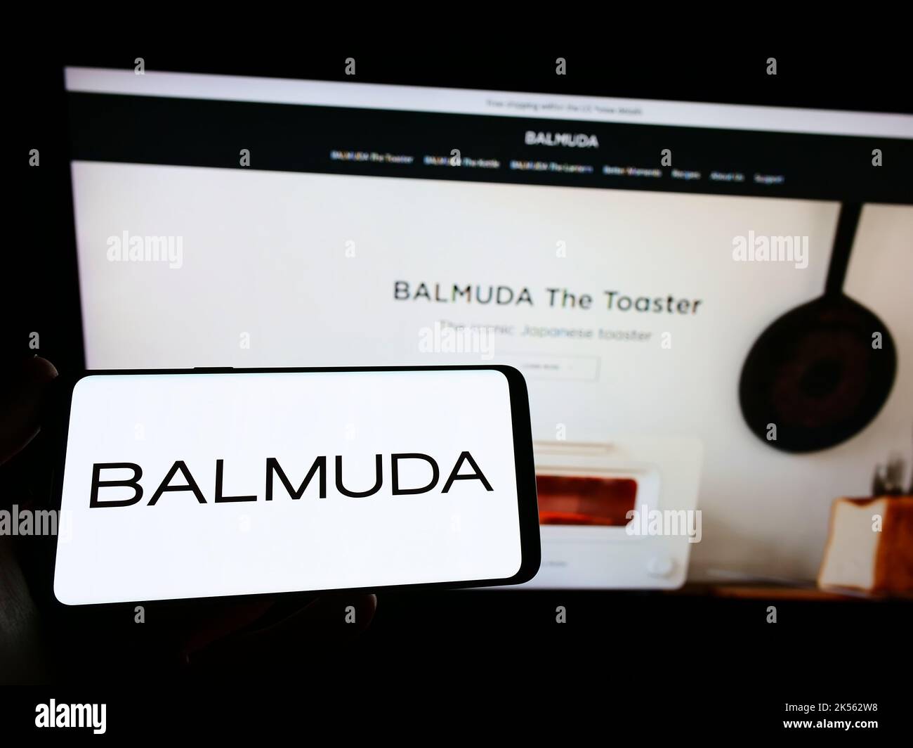 Person holding smartphone with logo of Japanese design company Balmuda K.K. on screen in front of website. Focus on phone display. Stock Photo