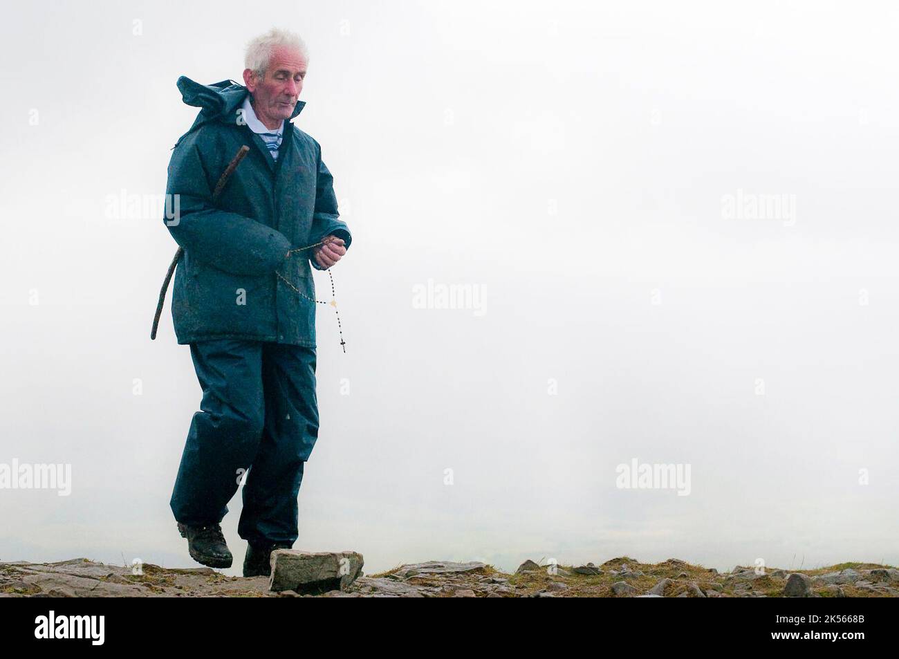 A man says the rosary while holding rosary beads on the summit of Croagh Patrick on Reek Sunday, when Roman Catholic pilgrims climb to the top to follow the steps of Saint Patrick. Stock Photo