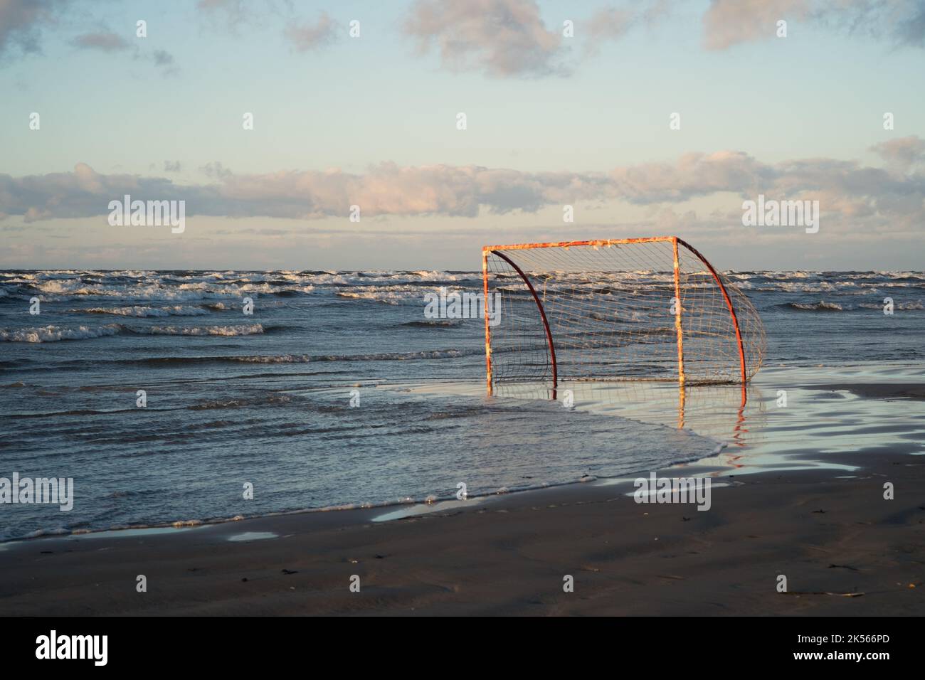 Advancing waves surround a beach football soccer goal in warm sunset light on baltic sea coast Stock Photo