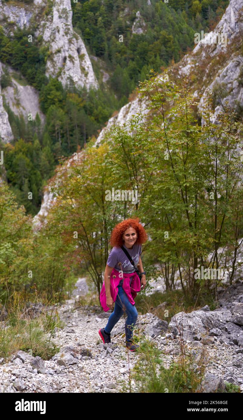 Tourist woman with curly hair with camera hiking on a steep trail in ...