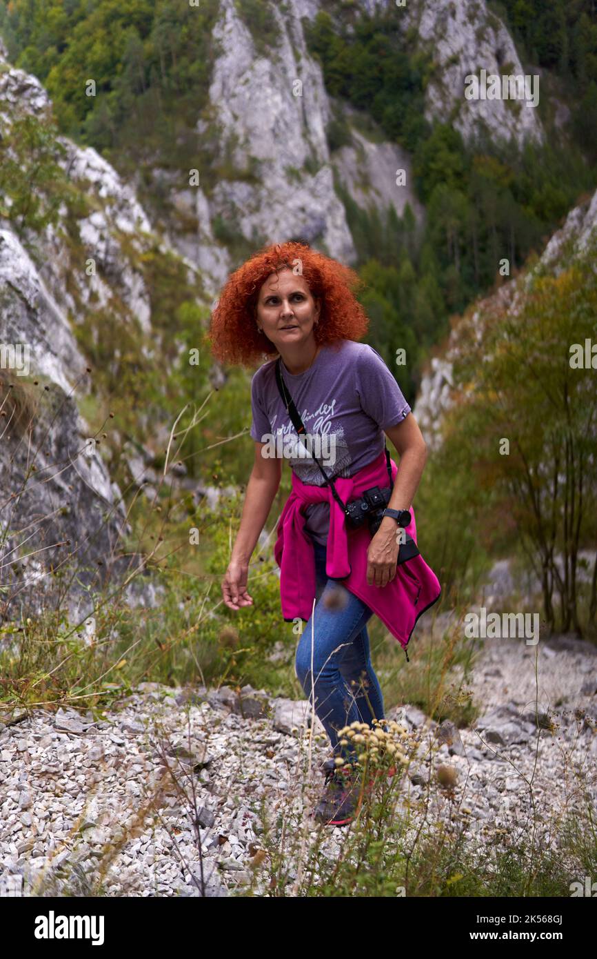 Tourist woman with curly hair with camera hiking on a steep trail in ...