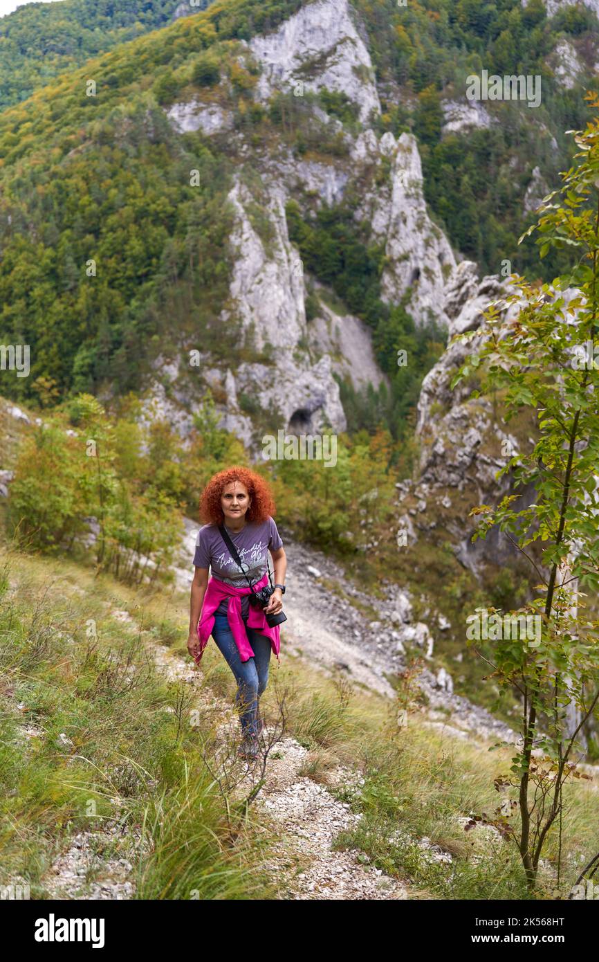 Tourist woman with curly hair with camera hiking on a steep trail in ...