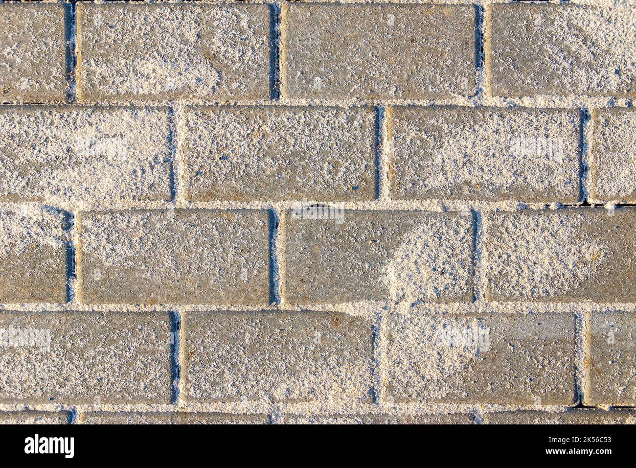Horizontal texture of paving slabs made of artificial stone or concrete is laid and seams are covered with sand, the remains of which are on the surfa Stock Photo