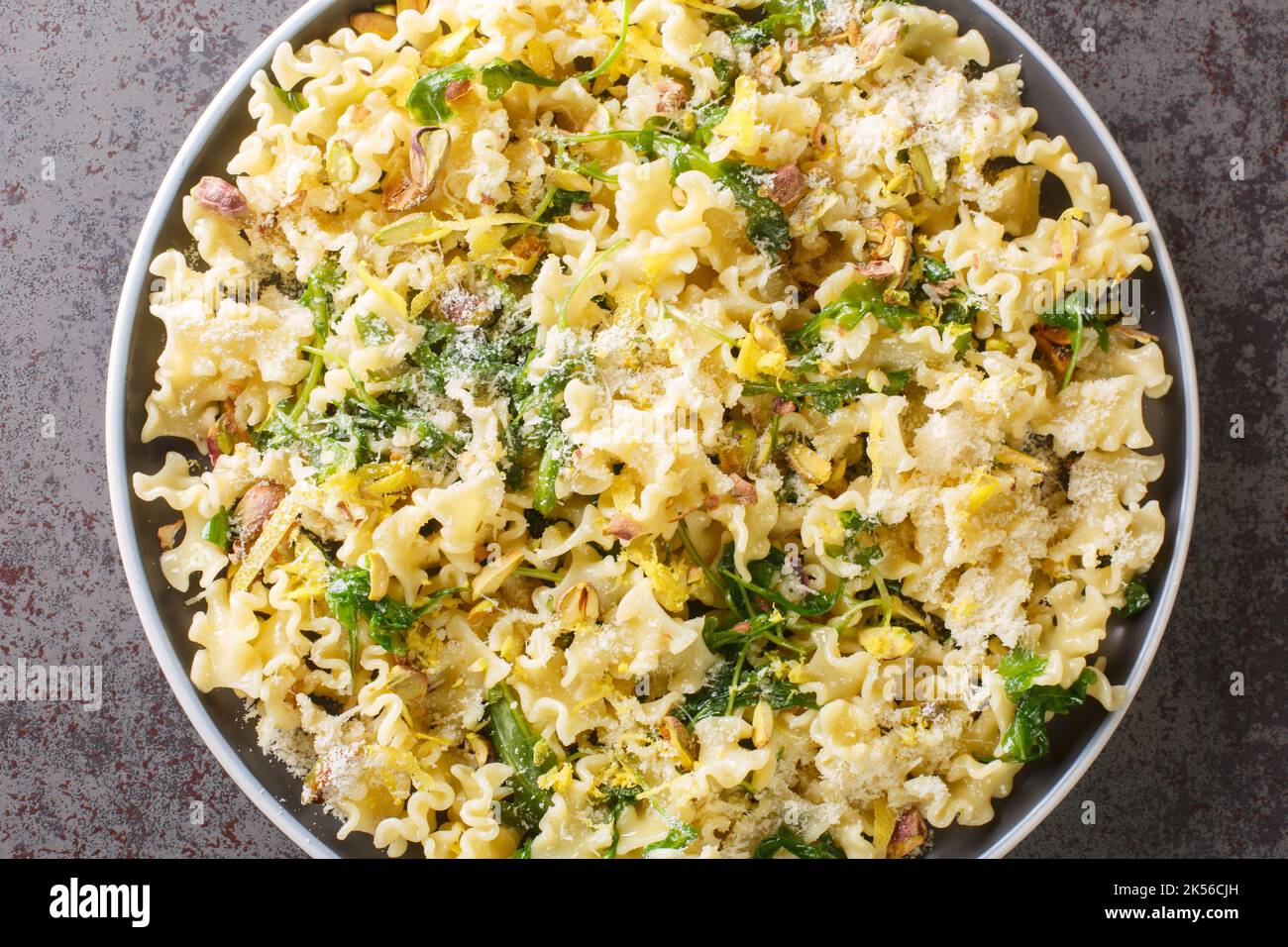 Mafalda pasta salad with arugula, roasted pistachios, parmesan cheese and lemon zest close-up on a plate on the table. horizontal top view from above Stock Photo