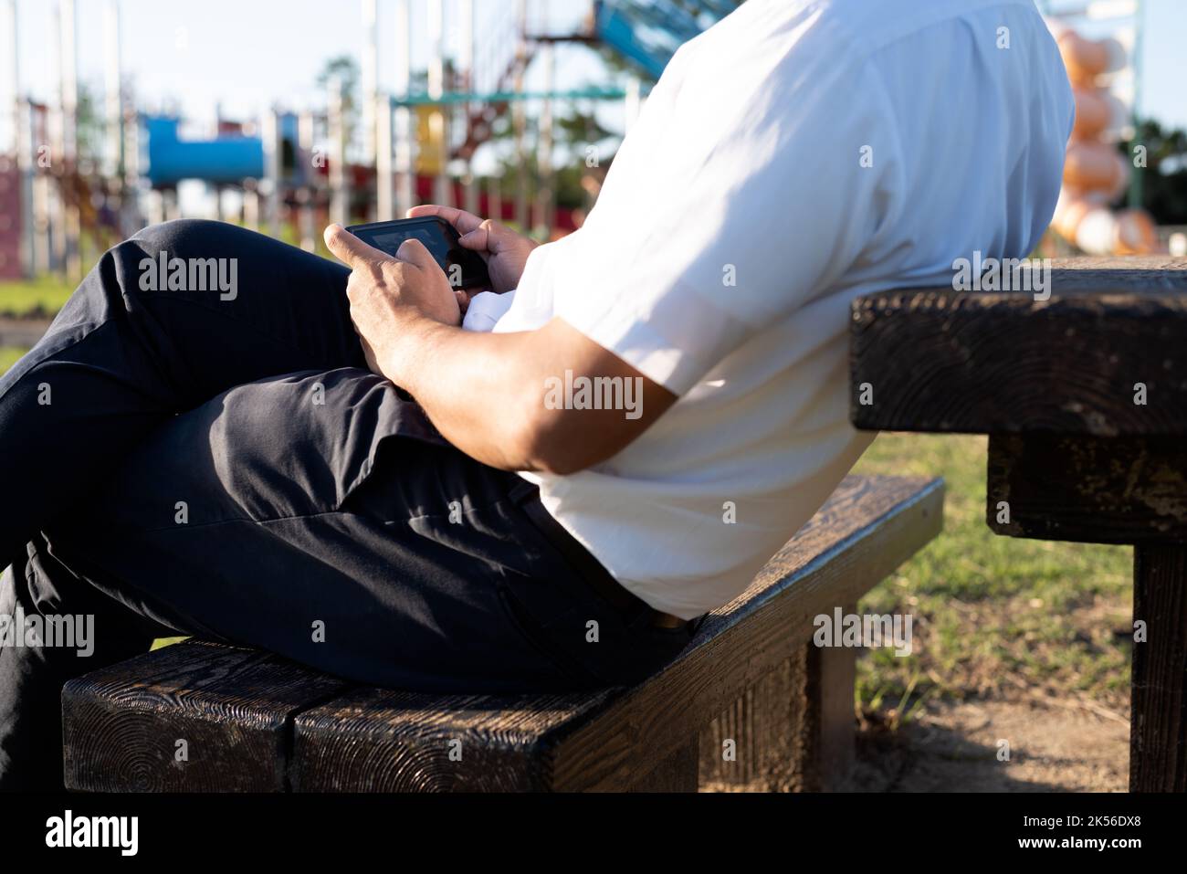 A man playing mobile phone games or smartphone game and sitting on a bench during sunset. Stock Photo