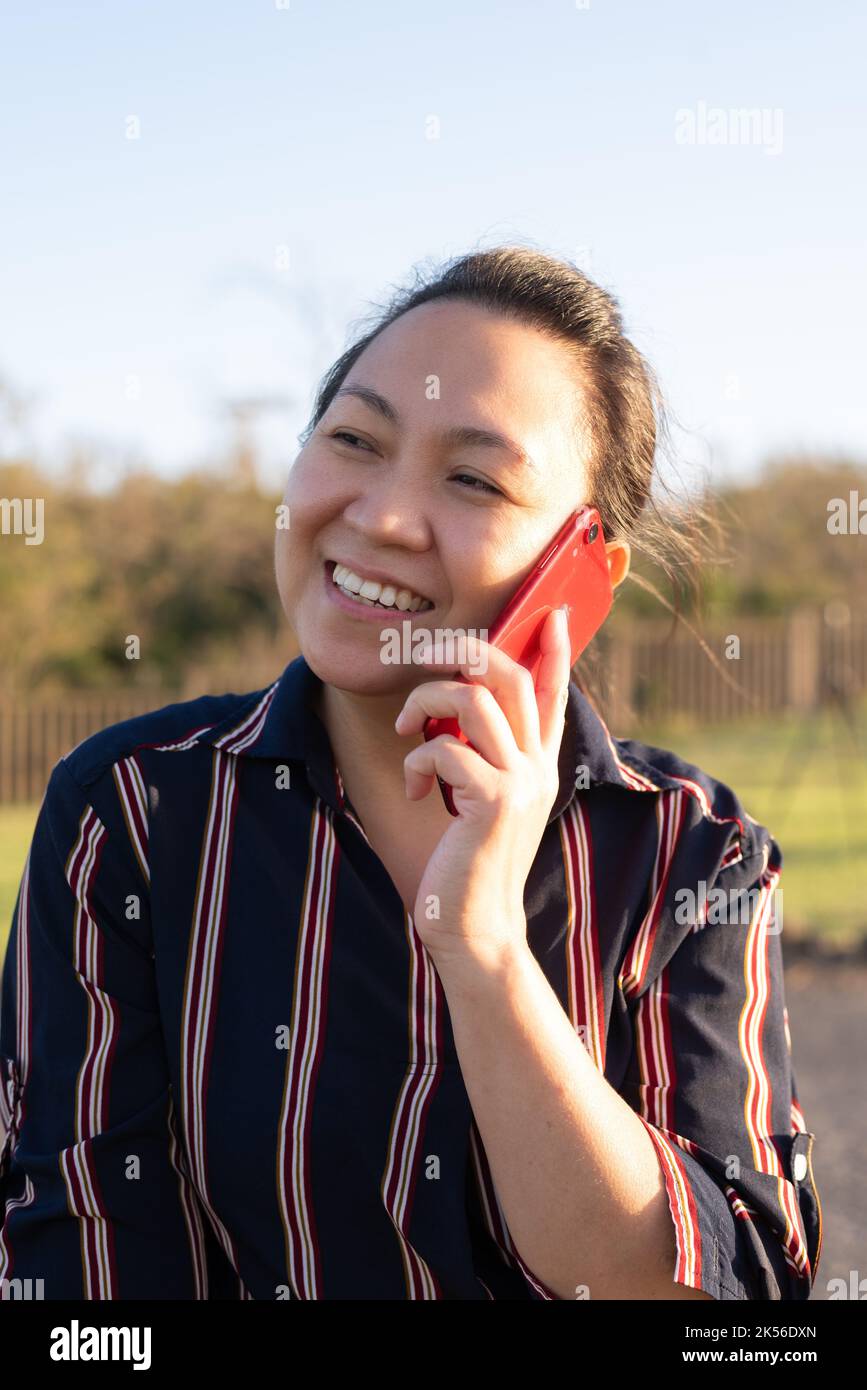 An Asian Filipino woman happily talks on the phone during sunset. Close-up shot portrait Stock Photo