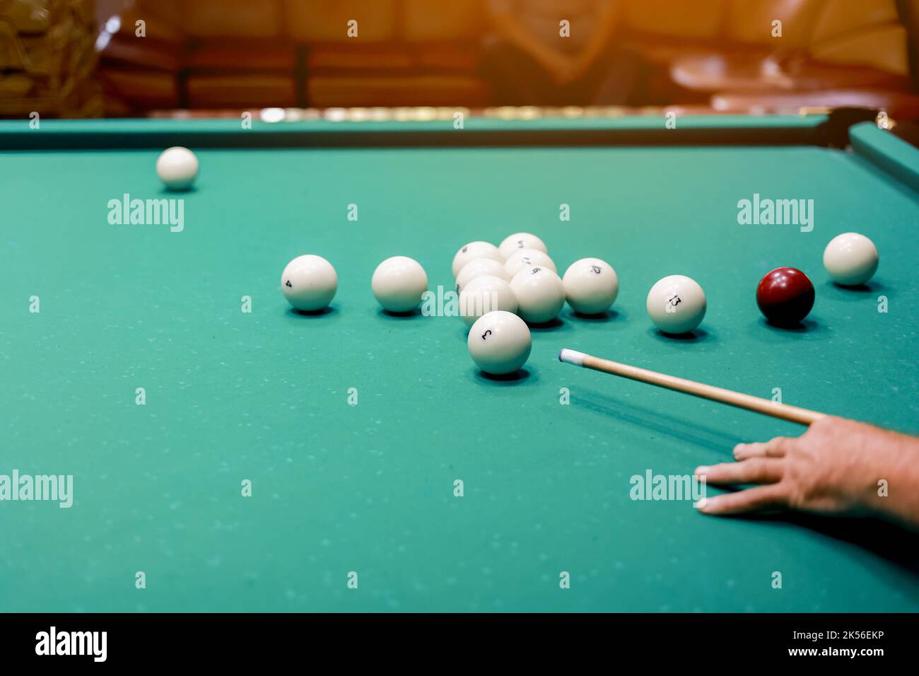 Playing billiards, close up of a mans hand with a cue hitting a white ball. Balls with numbers