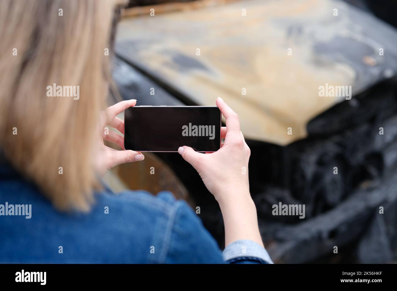 Insurance agent woman photographs burned-out car on smartphone Stock Photo