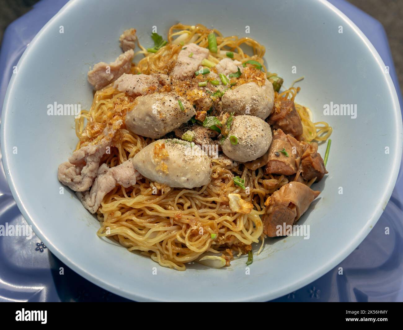 Egg Noodles with braised pork (stewed pork), fresh pork and pork balls without soup sprinkled with pepper and chopped onions in blue bowl. Selective f Stock Photo