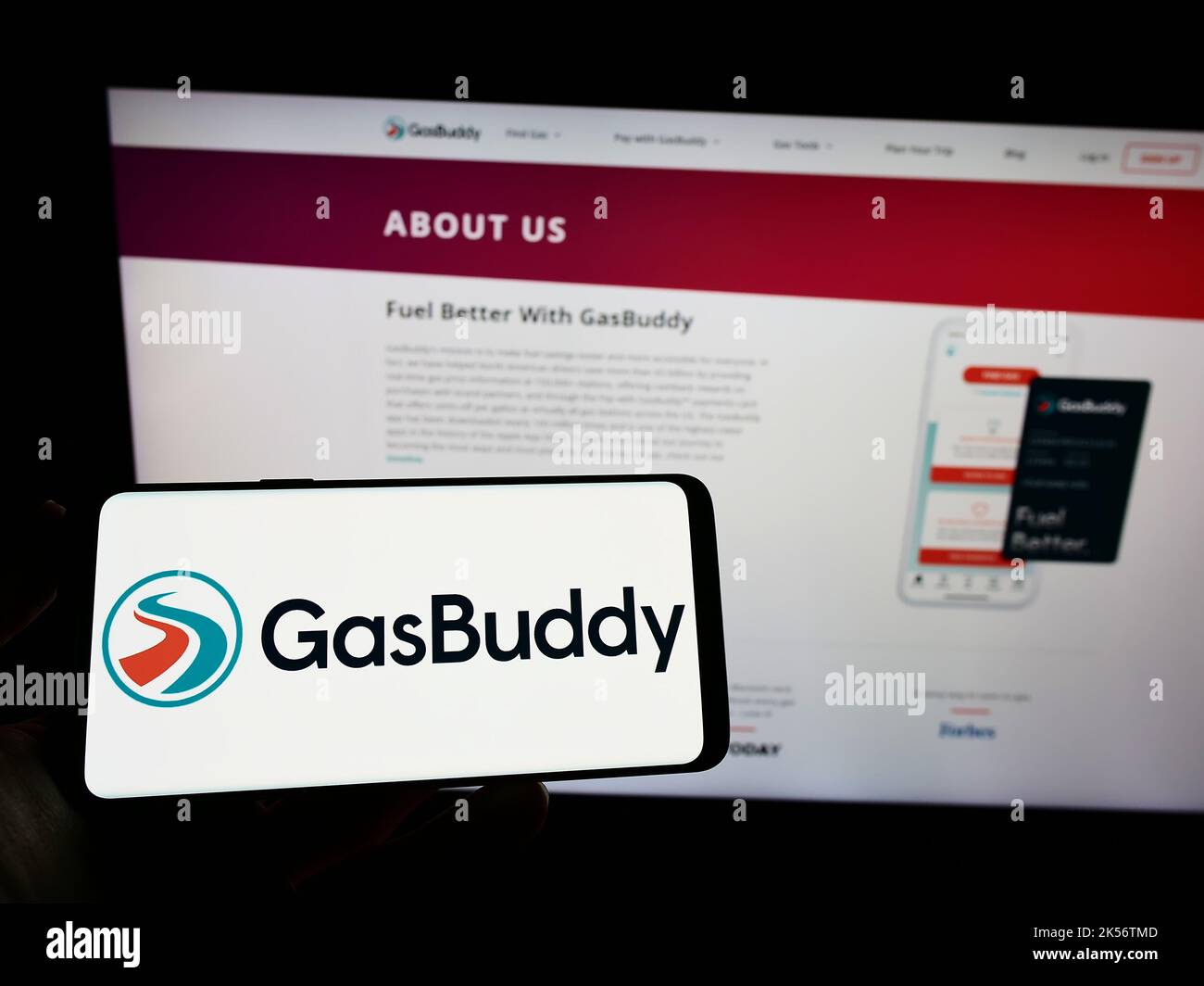 Person holding mobile phone with logo of American fuel pricing company GasBuddy LLC on screen in front of web page. Focus on phone display. Stock Photo