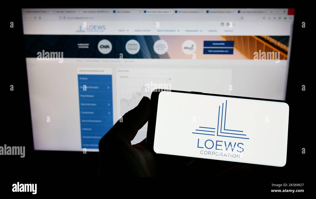 Person holding mobile phone with logo of American conglomerate Loews Corporation on screen in front of company web page. Focus on phone display. Stock Photo
