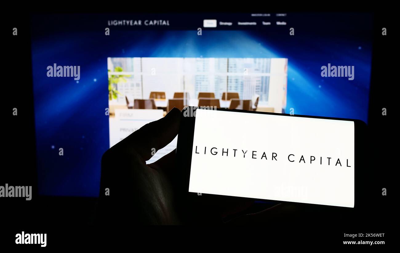 Person holding cellphone with logo of American private equity company Lightyear Capital on screen in front of webpage. Focus on phone display. Stock Photo