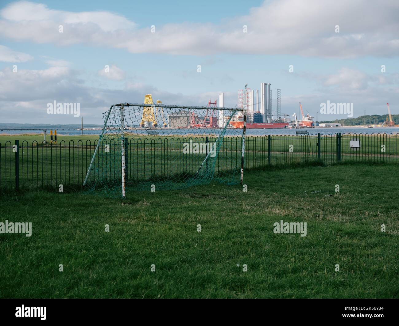 A lone football pitch goal and distant wind turbine factory in Cromarty, Black Isle, Ross & Cromarty, Highland, Scotland UK Stock Photo