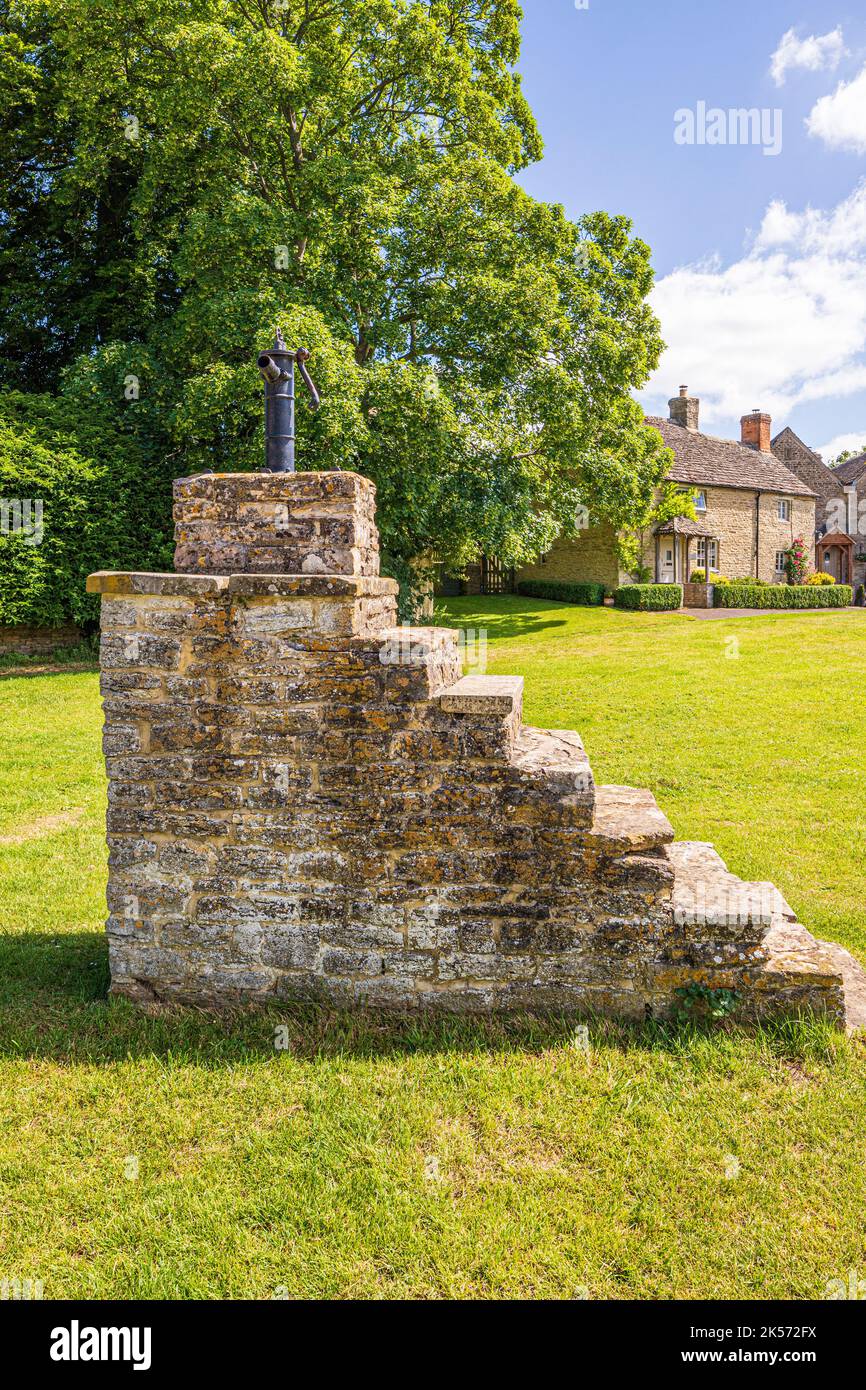 A cast iron water pump on top of a tall stone mounting block on the green in the Cotswold village of Meysey Hampton, Gloucestershire, England UK Stock Photo