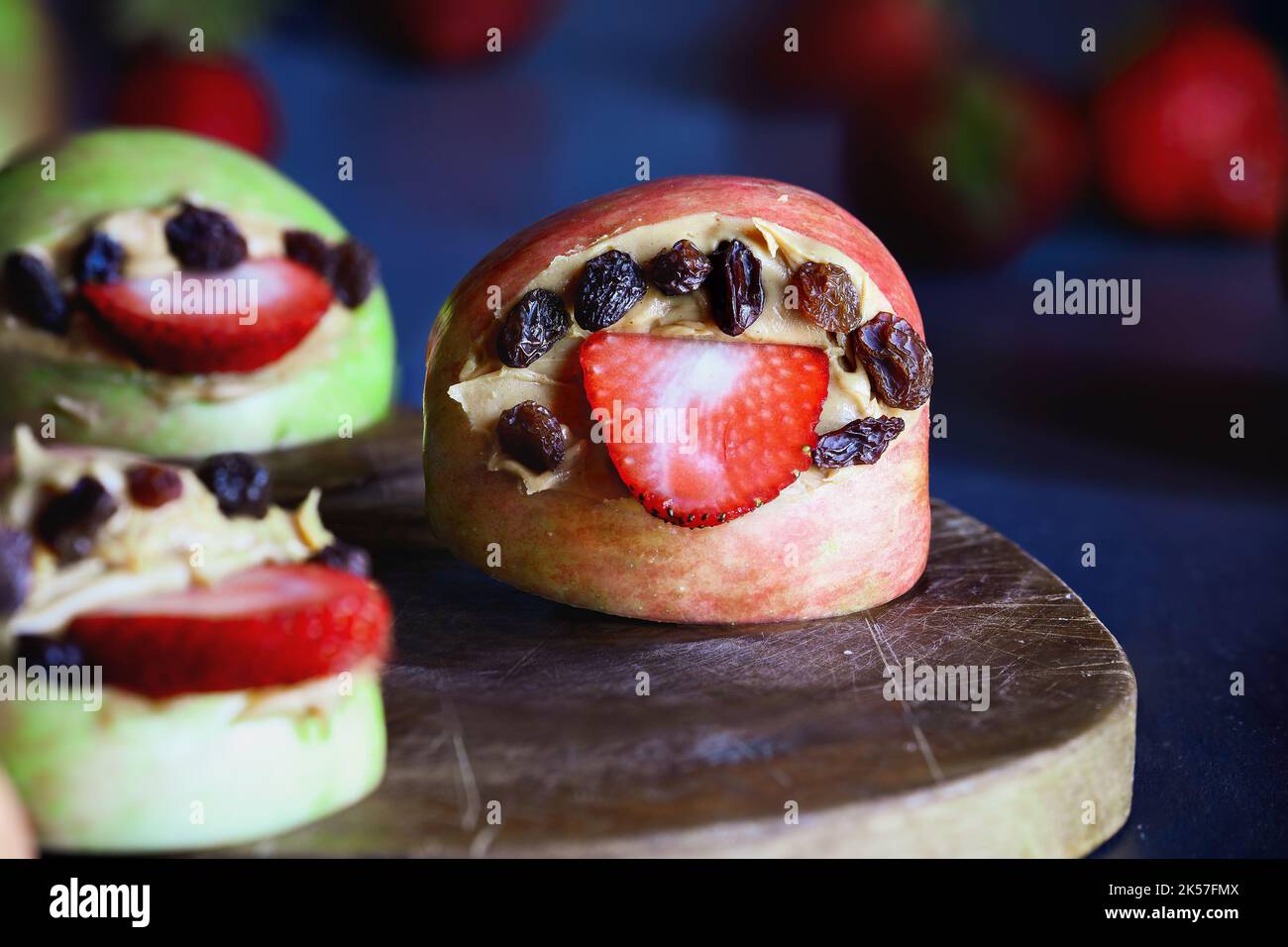 Apple monster mouths open wide with strawberry tongues and raisin teeth. Filled with peanut butter. Selective focus with blurred background. Stock Photo