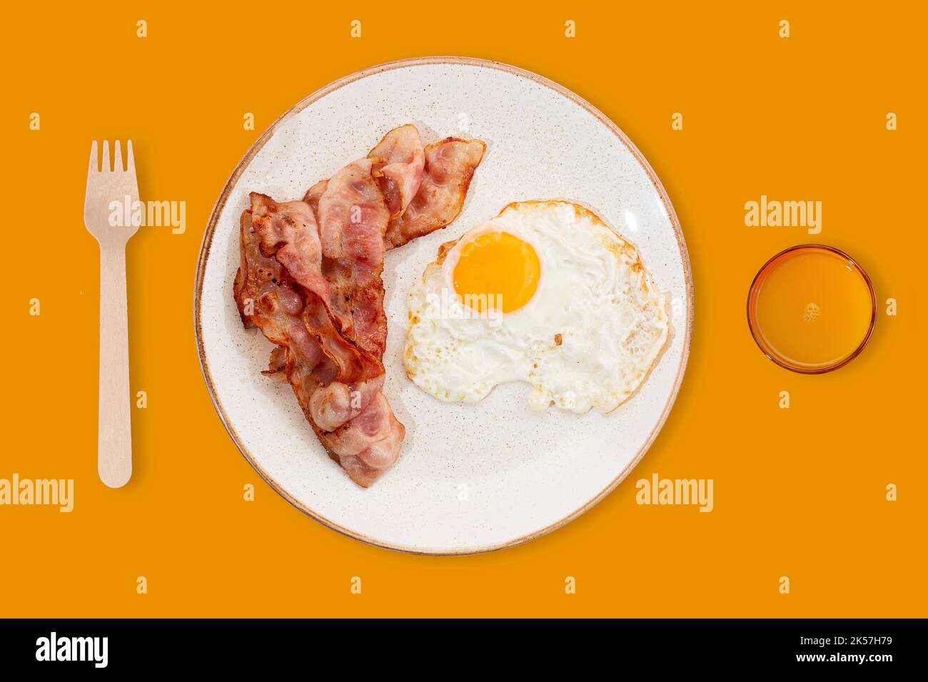 The best breakfast. Bacon, a fried egg, and orange juice. Photo on a summer yellow background. Place for text. Marketing and advertising idea. Modern Stock Photo