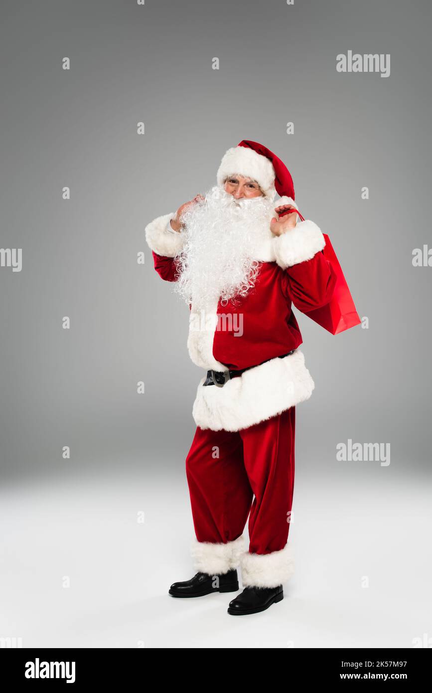 Full length of father christmas in costume holding shopping bag while standing on grey background,stock image Stock Photo