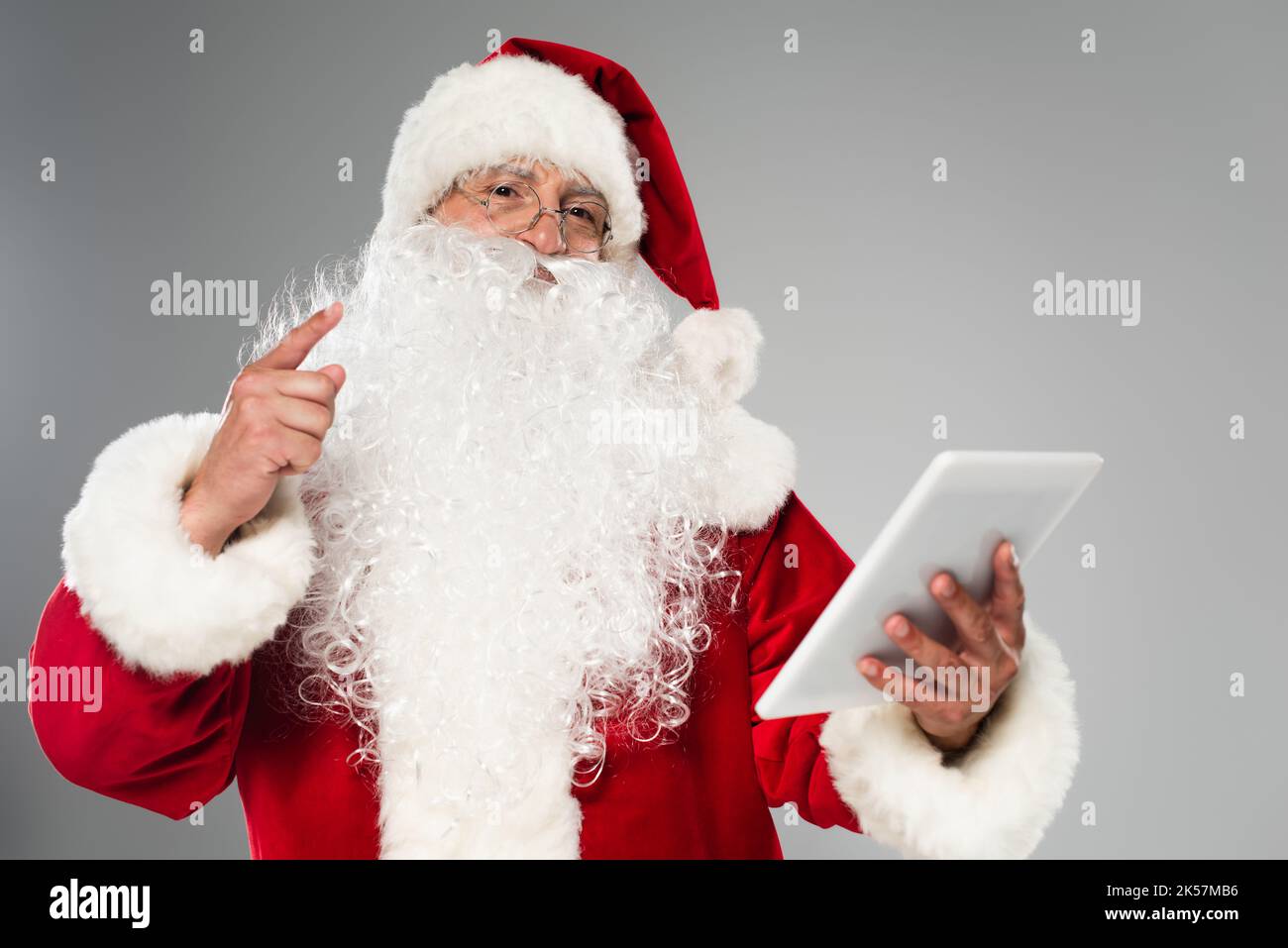 Father christmas in eyeglasses pointing with finger and holding digital tablet isolated on grey,stock image Stock Photo