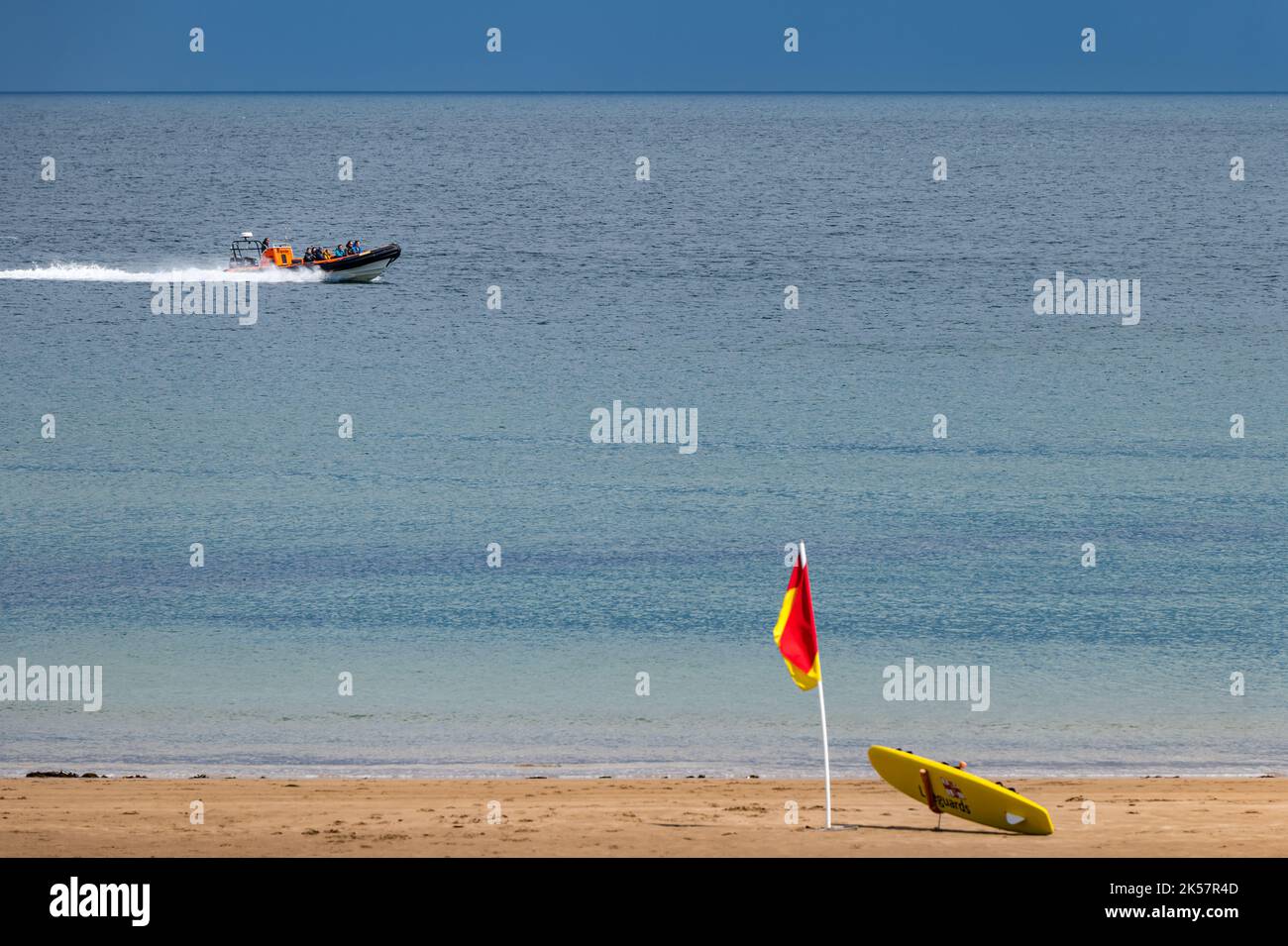 Tourists in a rigid inflatable boat in Summer weather, near beach with lifeguard flag Coldingham Bay, Berwickshire, Scotland, UK Stock Photo