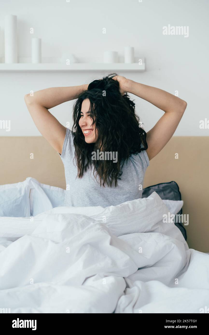 Morning energy. Home weekend. Fresh start motivation. Happy inspired brunette woman stretching smiling in bed in bedroom with sunlight. Stock Photo