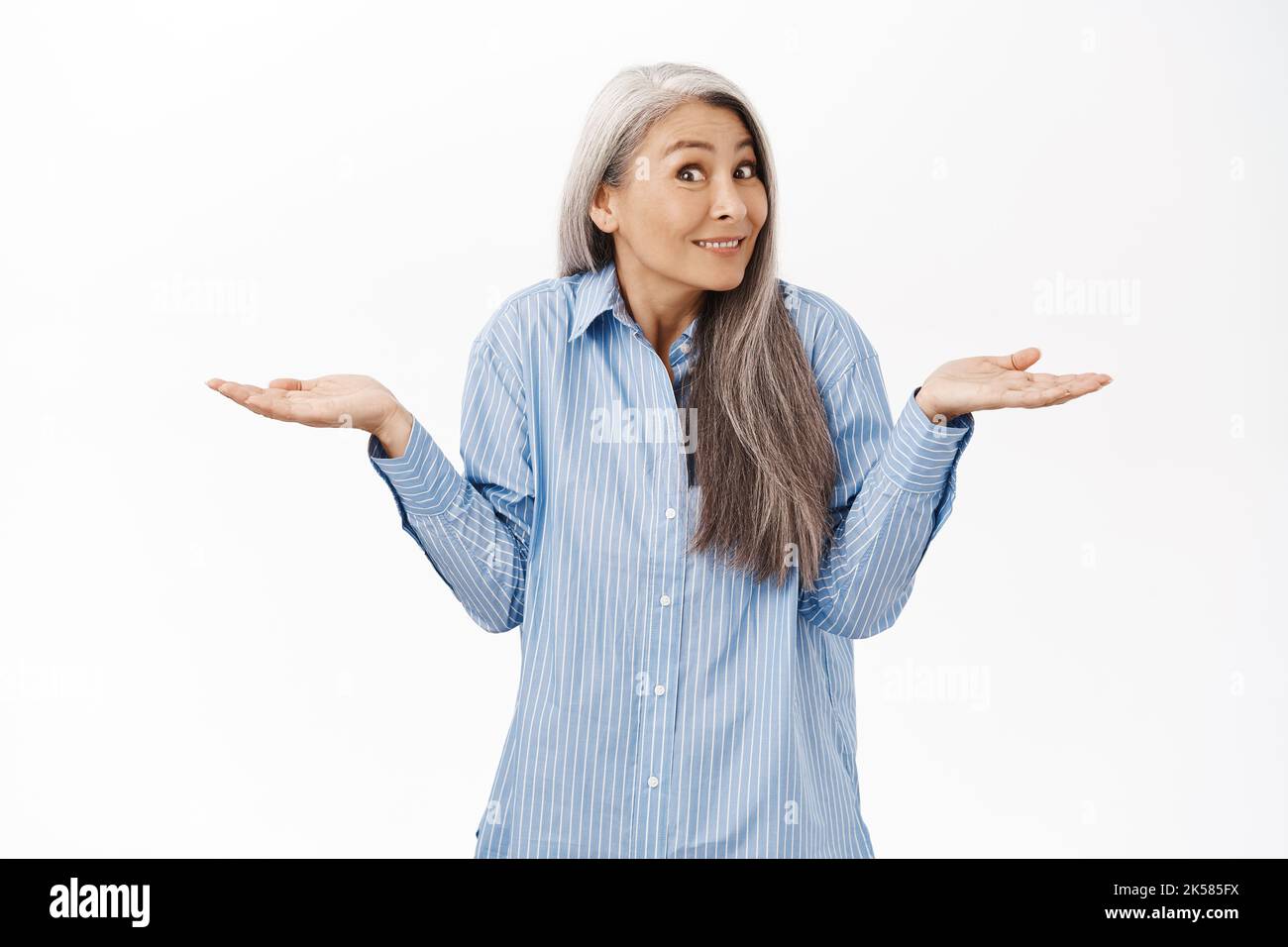 Dont know. Clueless asian lady shrugging shoulders and smiling. Senior japanese woman looking puzzled, standing over white background Stock Photo