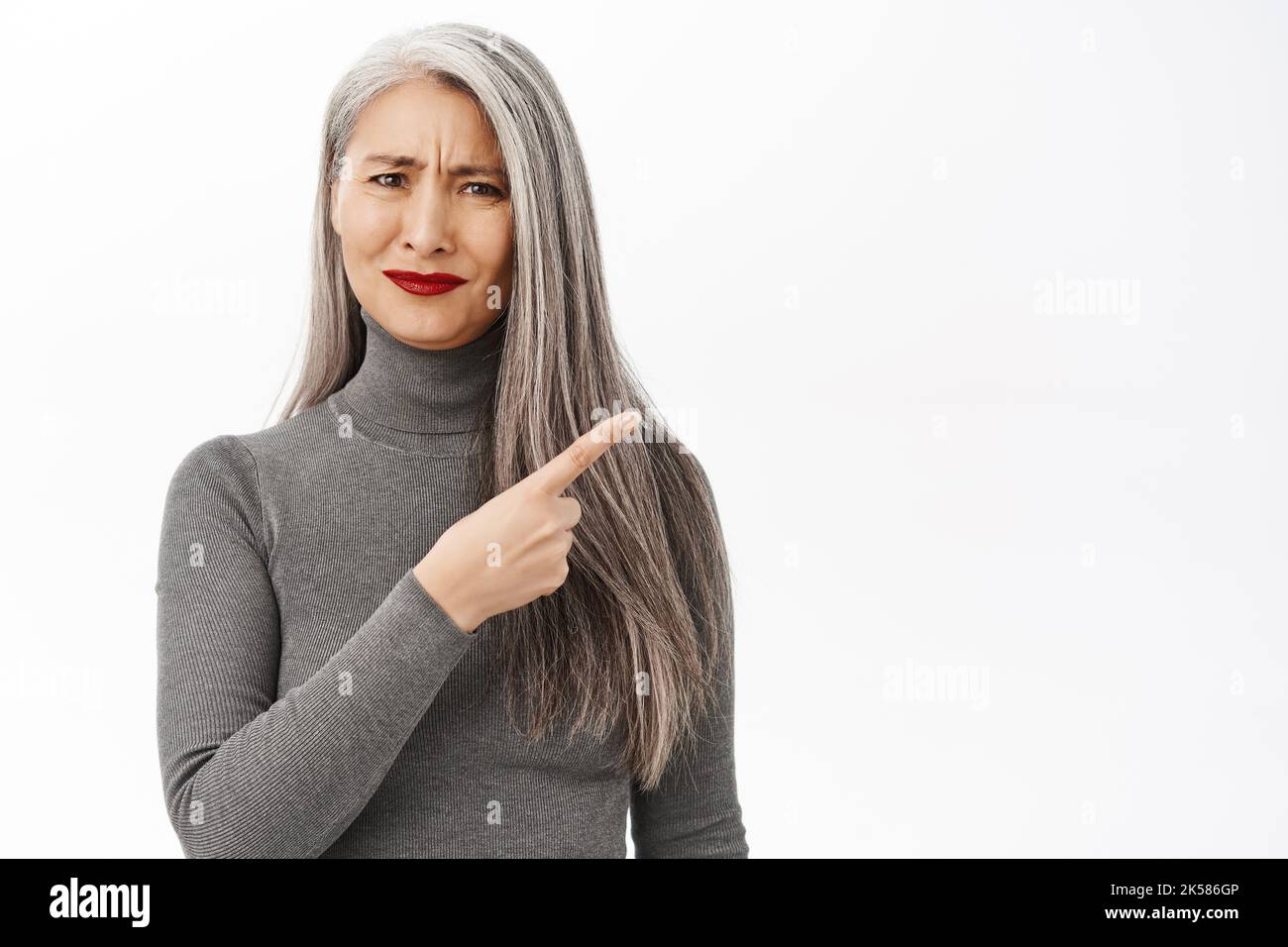Portrait of confused asian senior woman frowning, pointing right at ...