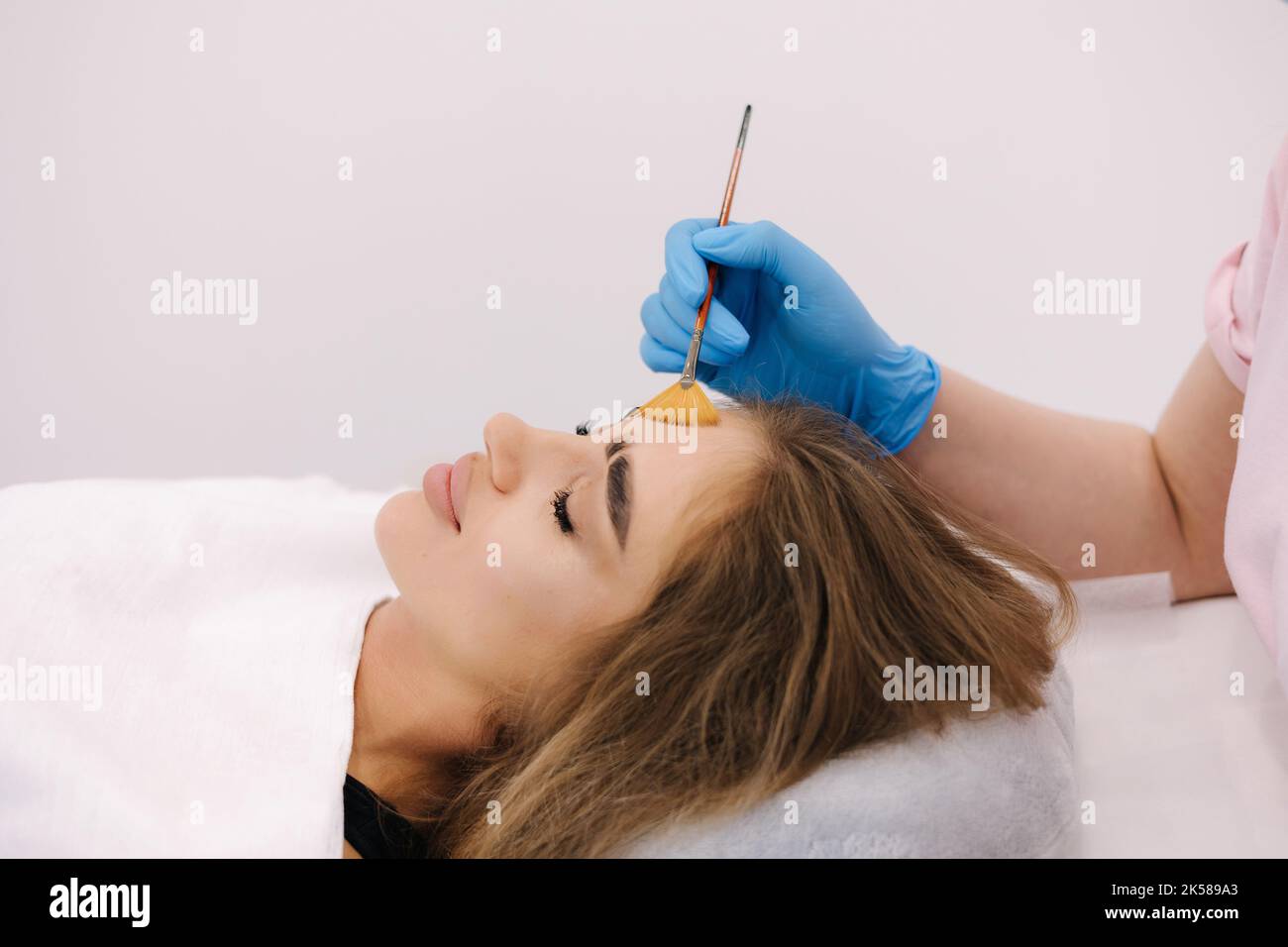 Young woman cosmetologist apply white clay mask on woman's face. Beautiful woman in beauty salon Stock Photo