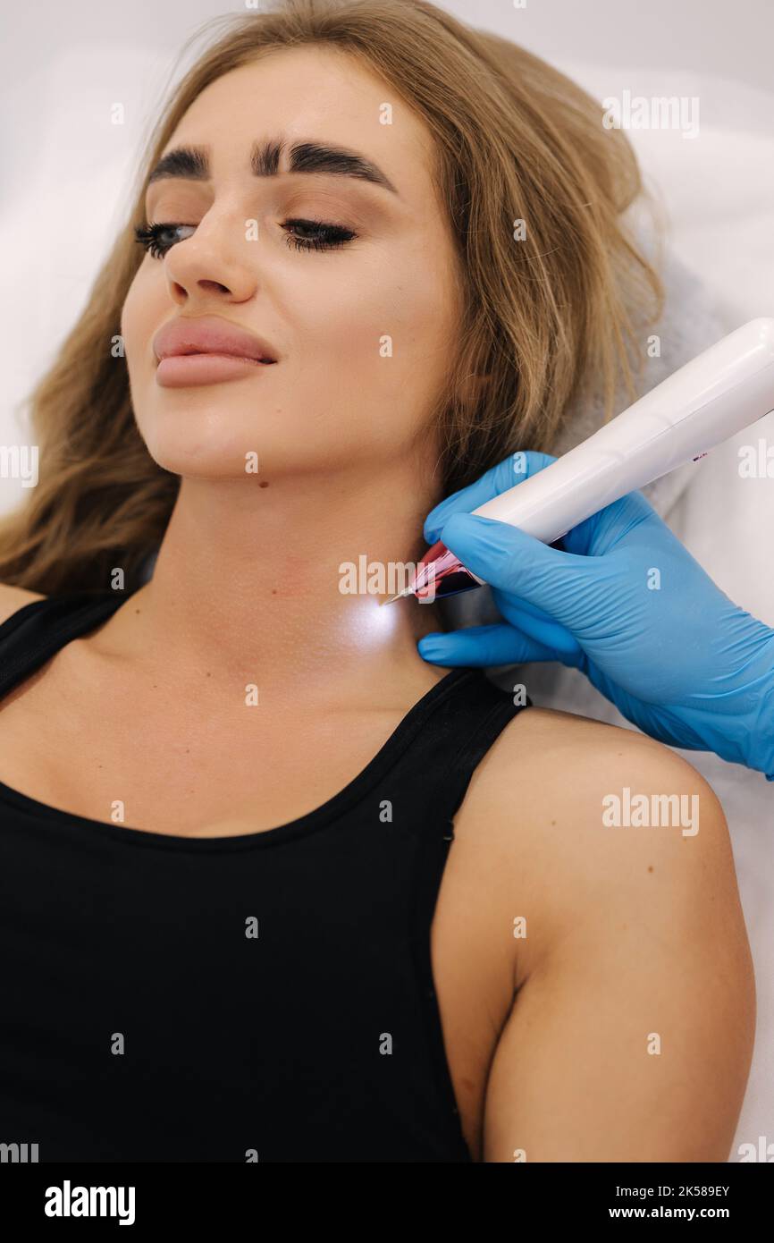 Plasma pen reducing neoplasm around neck on young woman. Woman at cosmetology clinic taking a beauty procedure for skin. Noninvasive cosmetic Stock Photo