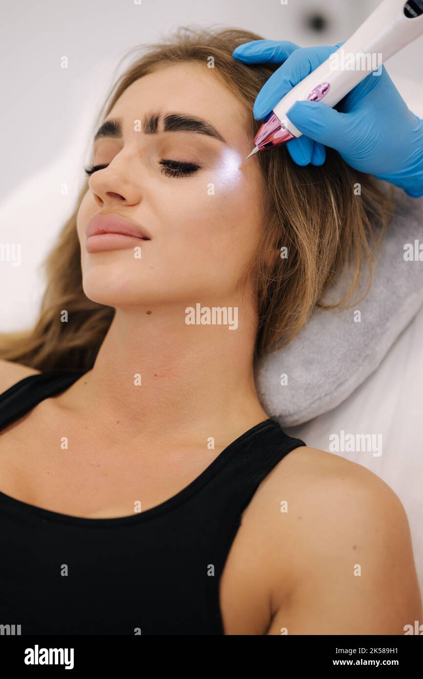 Plasma pen reducing wrinkles around eyes on young woman. Woman at cosmetology clinic taking a beauty procedure for skin. Noninvasive cosmetic Stock Photo
