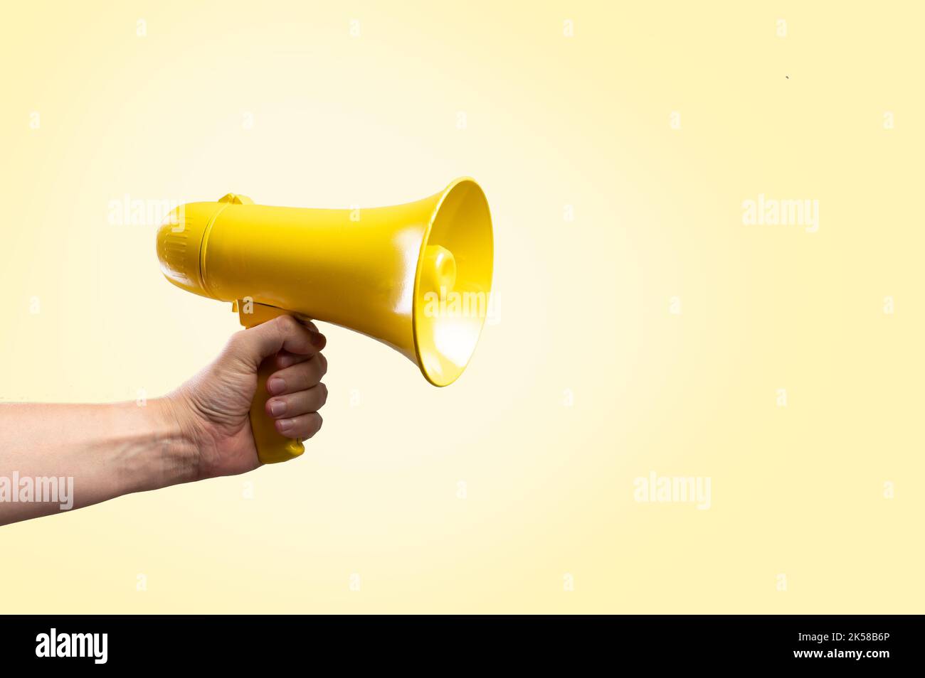 In the hand of a man is a yellow megaphone on a light beige background. Minimalism. Propaganda, rumors, journalism, media, business, election debates. Stock Photo