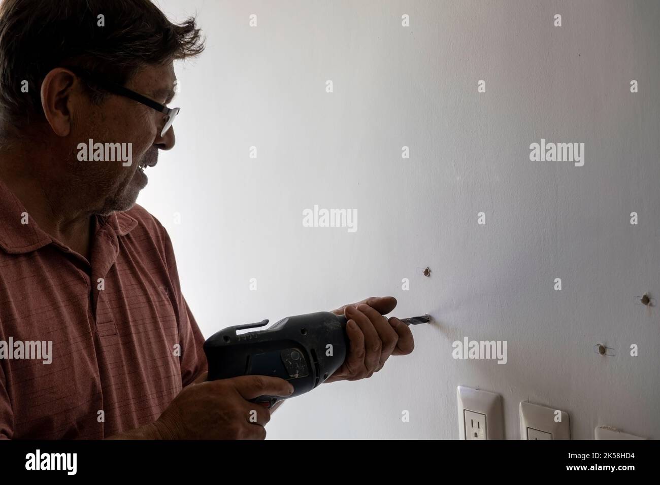 latino man using a power drill to drill holes in the wall to hang a new television, drilling holes in the wall, mexican, hispanic Stock Photo