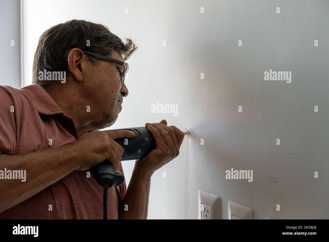 latino man using a power drill to drill holes in the wall to hang a new television, drilling holes in the wall, mexican, hispanic Stock Photo