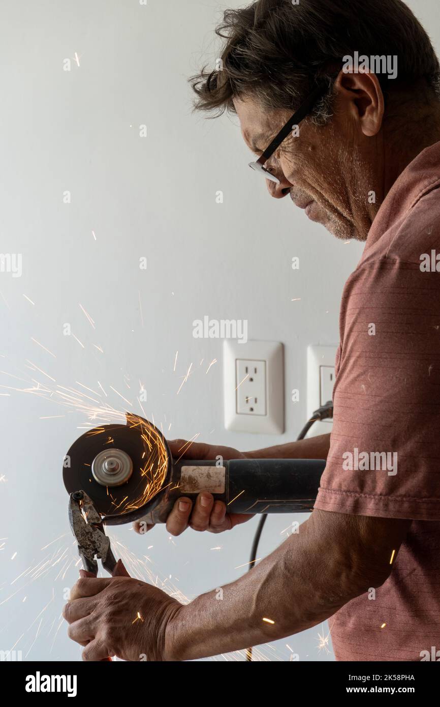 man using angle grinder, cutting a screw, friction sparks, clamping screw with tweezers concentration face and concern latino man Stock Photo