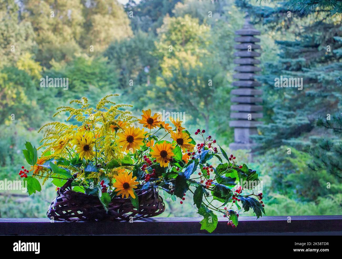Ikebana - composition of flowers with yellow flowers and red berries and green leaves on background of Japanese garden with stone lantern ( or maybe s Stock Photo